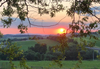Sunset over rolling hills seen from Holiday park «Jägerwiesen 1» in Germany, framed by tree branches.