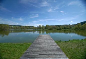 A wooden pier extends over a peaceful lake at Holiday park «Jägerwiesen 1» in Germany, with greenery.