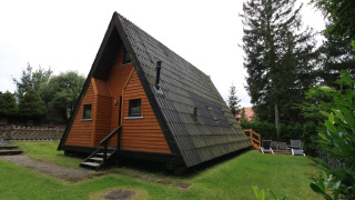 A-formet Nurdachhaus lodge med træbeklædning og skråt tag, omgivet af grøn græsplæne og træer.