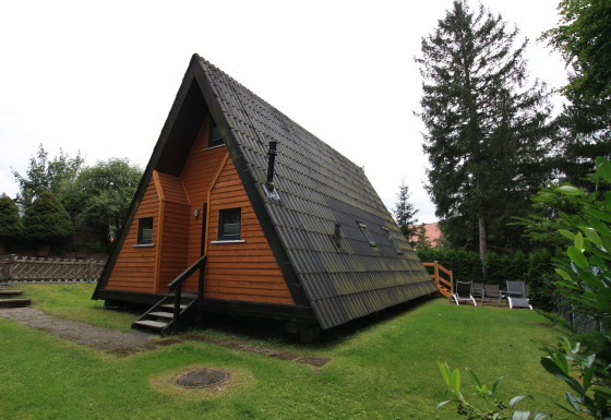 A-frame Nurdachhaus lodge with wood paneling and sloped roof, surrounded by green lawn and trees.