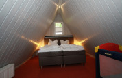 Loft bedroom in Type A1 Nurdachhaus lodge in Germany with double bed, angled walls, and baby cot.