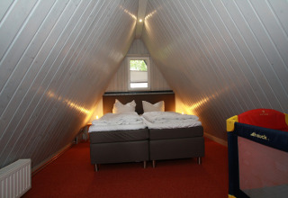 Loft bedroom in Type A1 Nurdachhaus lodge in Germany with double bed, angled walls, and baby cot.