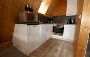 Küche im Holzhaus mit weißen Schränken, Mikrowelle, Spülmaschine, Backofen, Kaffeemaschine und Holzdecken.