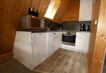 Küche im Holzhaus mit weißen Schränken, Mikrowelle, Spülmaschine, Backofen, Kaffeemaschine und Holzdecken.