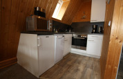 Kitchen in wooden lodge with white cabinets, microwave, dishwasher, oven, coffee maker, and sloped ceiling.