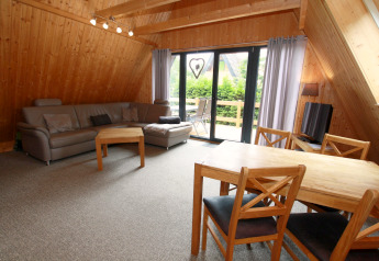 Soggiorno in un lodge di legno con divano grigio, tavolo da pranzo, sedie e vista sul balcone verde.