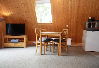 Woonruimte in een lodge met houten wanden, tafel en stoelen, tv, raam, koelkast en magnetron.