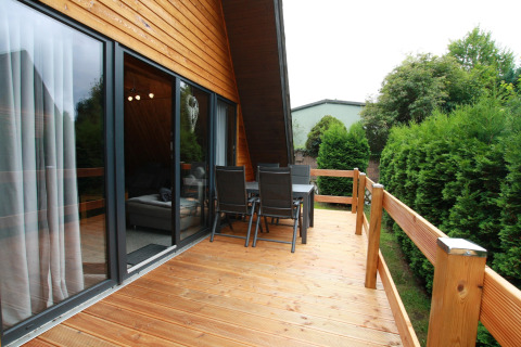 Wooden terrace with outdoor dining furniture at Type A1 - Nurdachhaus lodge in Germany, surrounded by greenery.