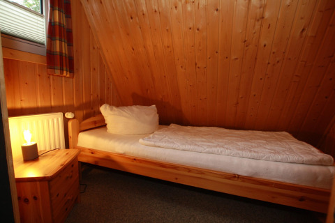 Cozy single room with wood panel walls, single bed, and nightstand at Type A1 - Nurdachhaus, Germany.