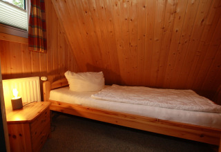 Cozy single room with wood panel walls, single bed, and nightstand at Type A1 - Nurdachhaus, Germany.