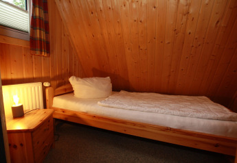 Cozy single room with wood panel walls, single bed, and nightstand at Type A1 - Nurdachhaus, Germany.