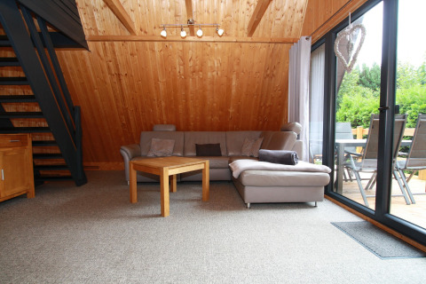 Gezellige lodge woonkamer met houten wanden, grijze hoekbank, tafeltje en uitzicht op groene terras.