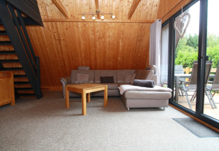 Knusse woonkamer in lodge met houten muren, grijze sofa, houten tafel en zicht op groen terras.