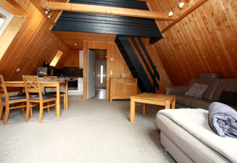 Interno di un lodge accogliente con pareti in legno, cucina aperta, tavolo da pranzo, divano e scala per il soppalco.