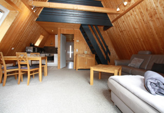 Gezellige lodge met houten bekleding, open keuken, eetgedeelte, zithoek en trap naar de mezzanine.