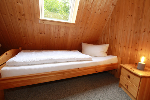 Knusse lodgekamer met eenpersoonsbed, houten wanden, raam, nachtkastje en sfeerlampje.