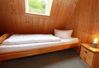 Knusse lodgekamer met eenpersoonsbed, houten wanden, raam, nachtkastje en sfeerlampje.