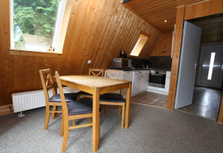 Wood-paneled dining and kitchen area in Nurdachhaus, Germany, with table, four chairs, and skylight windows.