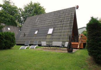 Afbeelding van een A-frame lodge met ligstoelen, banken, vuurkorf en terras in een groene tuin.