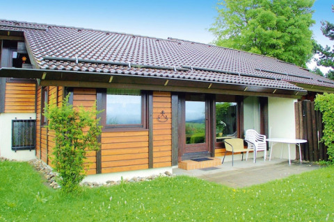 Chalet au village de vacances Öfingen, 68 m² Type C Sioux, extérieur bois, terrasse avec chaises et table.