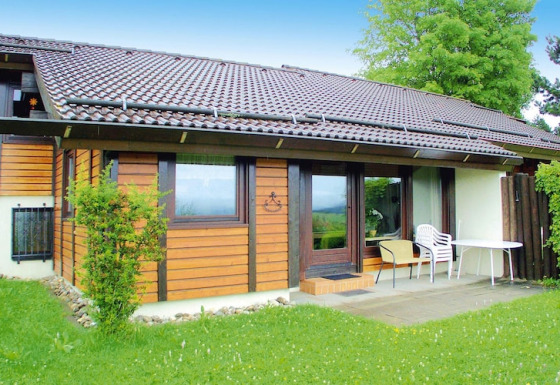 Chalet at Holiday village Öfingen, 68 sqm Type C Sioux, wooden exterior, patio with chairs and table.