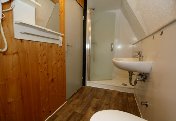 Bagno di un lodge con pareti in legno, box doccia, lavabo sospeso, specchio e pavimento in legno.