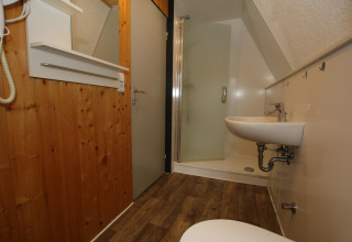 Lodge bathroom with wood panel walls, shower cubicle, wall-mounted sink, mirror, and wooden flooring.