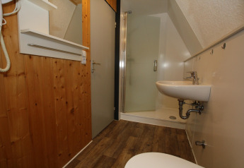 Badkamer in een lodge met houten wand, douchecabine, wasbak, spiegel en warme houten vloer.