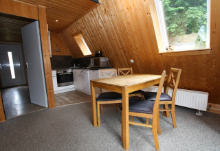 Interior of Type A1 - Nurdachhaus lodge in Germany with wood paneling, dining table, and kitchen area.