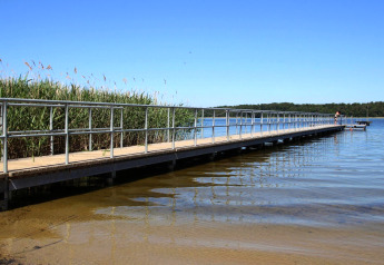 Long ponton avec rambarde au bord du lac près du lodge Type A1 - Nurdachhaus en Allemagne, ciel dégagé.