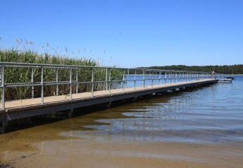 Long pier with railing by the lake at Type A1 - Nurdachhaus lodge in Germany, under a clear blue sky.