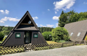 Casa vacanze A-frame in legno con finestre verdi e giardino, fotografata in Germania con cielo sereno.