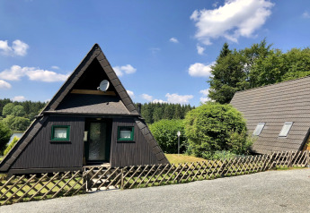 Casa vacanze A-frame in legno con finestre verdi e giardino, fotografata in Germania con cielo sereno.