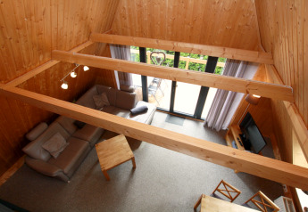 Salon avec murs et poutres en bois, grandes fenêtres vu d'en haut dans un lodge Nurdachhaus type A en Allemagne.