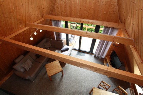 Woonkamer met houten wanden, balken en grote ramen in Nurdachhaus lodge in Duitsland, van bovenaf gezien.