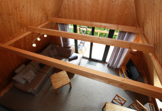 Living room with wood walls, beams, and large windows in Type A Nurdachhaus lodge in Germany, seen from above.
