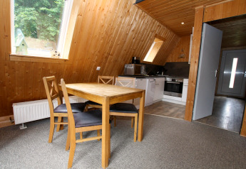 Intérieur d’un lodge Nurdachhaus en Allemagne avec table à manger, chaises, murs boisés et coin cuisine.