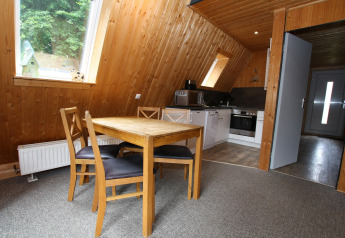 Interior of Type A Nurdachhaus lodge in Germany with dining table, chairs, wood walls and kitchen area.