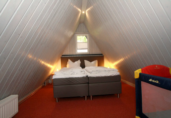 Chambre dans un lodge en A en Allemagne avec deux lits, moquette rouge et lit bébé dans un coin.