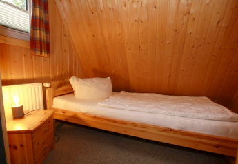 Chambre simple en bois avec lit, table de nuit et lampe dans un lodge Nurdachhaus en Allemagne.