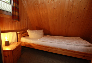 Knusse houten kamer met eenpersoonsbed, nachtkastje en lamp in Nurdachhaus, Duitsland.