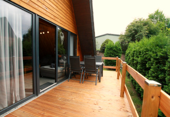 Terrasse en bois avec table et chaises à un lodge Nurdachhaus de type A en Allemagne, entourée de haies.