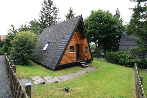 Knus Type A - Nurdachhaus lodge met houten gevel en zwart dak, omgeven door groene tuin in Duitsland.