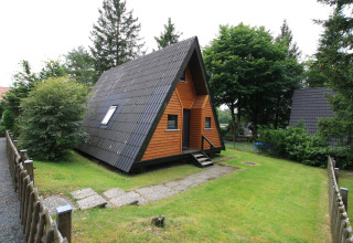Gezellige Type A - Nurdachhaus lodge met houten gevel en zwart dak, in een groene tuin in Duitsland.