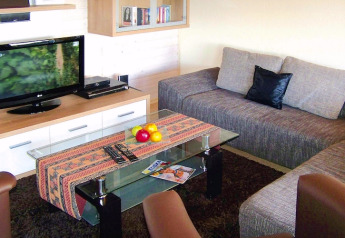 Salon du Holiday village Öfingen, Allemagne, avec canapé, table en verre, corbeille de fruits et télévision.