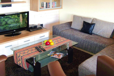 Sala de estar en Holiday Village Öfingen, Alemania, con sofá, mesa de vidrio, frutero y televisor en un chalet.