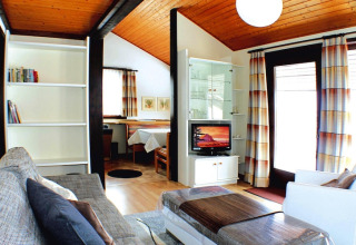 Salón del chalet en Holiday village Öfingen, Alemania, decoración moderna, techo de madera y grandes ventanas.