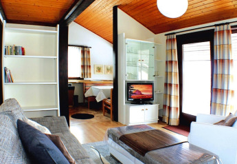 Living room in Holiday village Öfingen, Germany, featuring modern decor, wood ceiling, and large windows.
