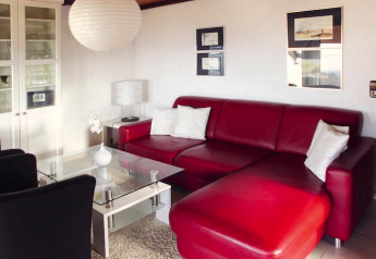 Salon moderne avec canapé en cuir rouge, table en verre et coussins blancs au Holiday village Öfingen, Allemagne.