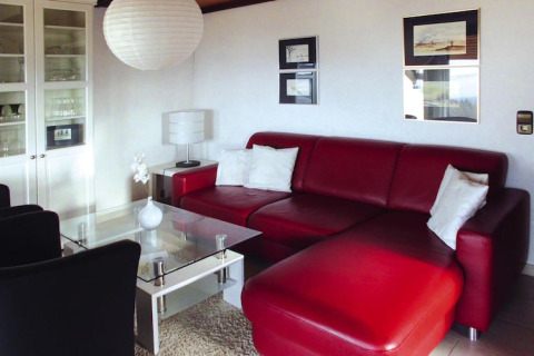 Soggiorno moderno con divano in pelle rossa, tavolo in vetro e cuscini bianchi al Holiday village Öfingen, Germania.